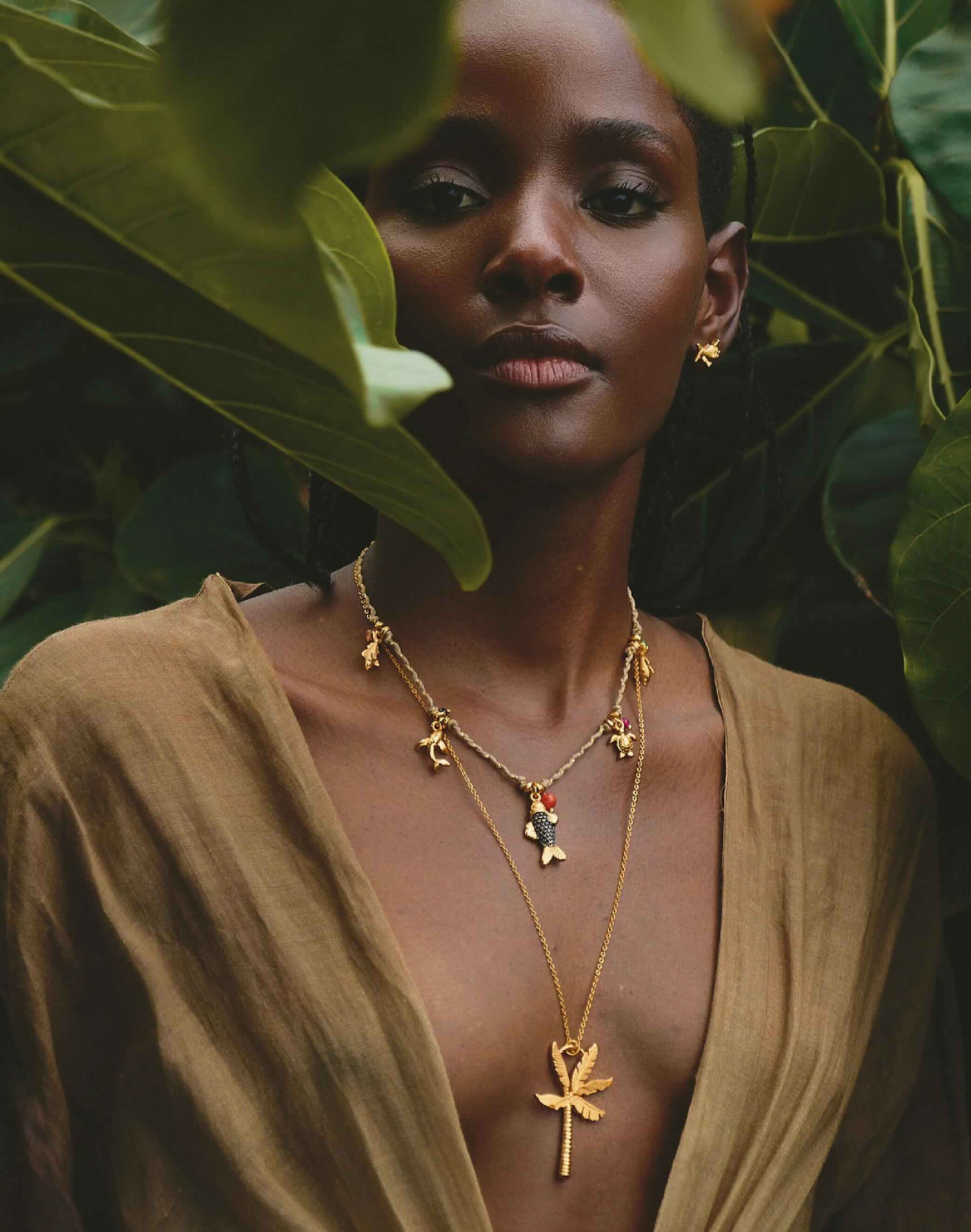 Woman wearing gold necklaces with palm tree pendants in a natural setting