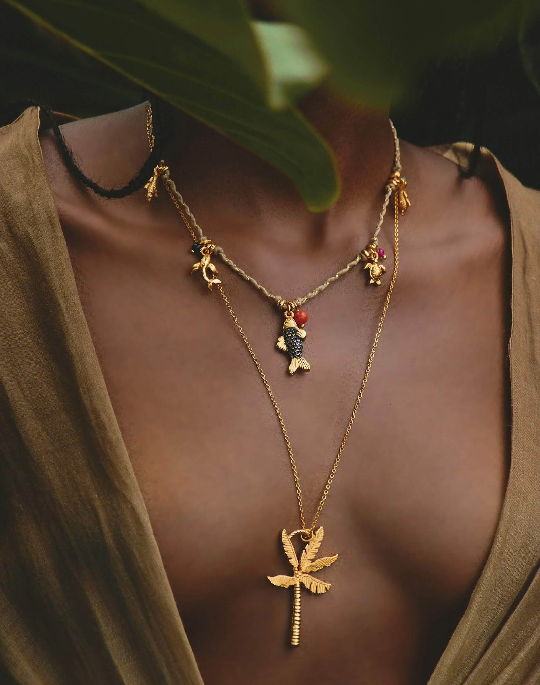 Gold necklace with leaf pendant worn by a woman, with a blurred background