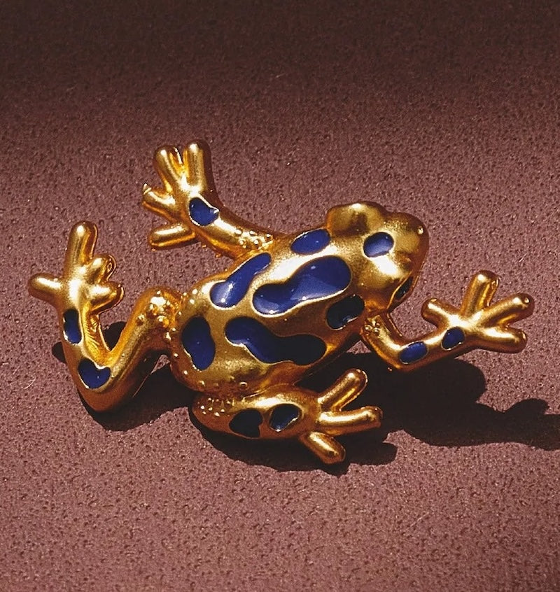 Gold frog brooch with blue spots on a brown background