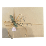 An image of how we gift wrap at EVAMAIA. Pictured is a kraft box, with a handmade wax stamp, a piece of eucalyptus and finished with a raffia ribbon bow.