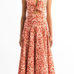 Woman wearing an orange and tan dress. She's standing on a white background. The purpose of this image is to highlight the dress by Encantadore Swim and Resortwear.