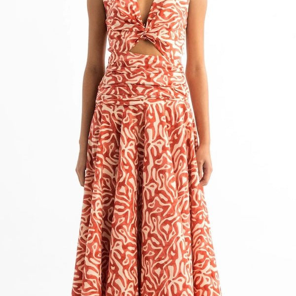 Woman wearing an orange and tan dress. She's standing on a white background. The purpose of this image is to highlight the dress by Encantadore Swim and Resortwear.