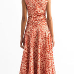 Back of a woman wearing an orange and tan dress. She's standing on a white background. The purpose of this image is to highlight the dress by Encantadore Swim and Resortwear.