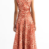Back of a woman wearing an orange and tan dress. She's standing on a white background. The purpose of this image is to highlight the dress by Encantadore Swim and Resortwear.