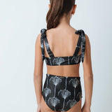 Back of a girl wearing a black and white bikini set. She's standing behind a white background. The purpose of this image is to highlight the swimsuit by Mar de Lua. 