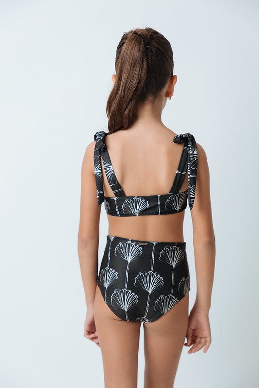 Back of a girl wearing a black and white bikini set. She's standing behind a white background. The purpose of this image is to highlight the swimsuit by Mar de Lua. 