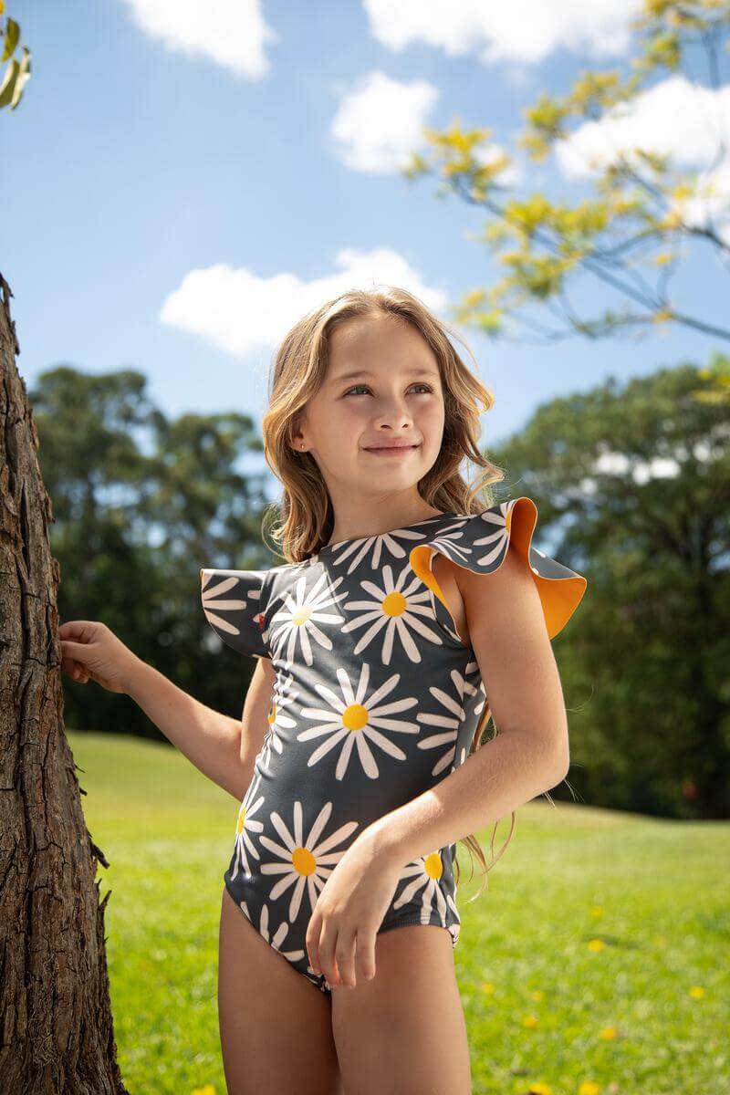 Little girl posing in the swimsuit at a park under a sunny day. She is smiling and looking away from the camera. 