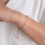 Close up image of a woman wearing a gold chain bracelet with an rose quartz stone on it. The purpose of the image is to highlight the bracelet because it is on sale at EVAMAIA boutique in Studio City, CA.