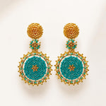 A pair of ornate handmade beaded drop earrings with gold-toned metal posts and circular turquoise, white, and gold beadwork, displayed on a clean off-white background.