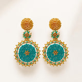 A pair of ornate handmade beaded drop earrings with gold-toned metal posts and circular turquoise, white, and gold beadwork, displayed on a clean off-white background.
