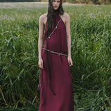 Woman in a long burgundy dress and red headscarf standing in a field of tall grass.