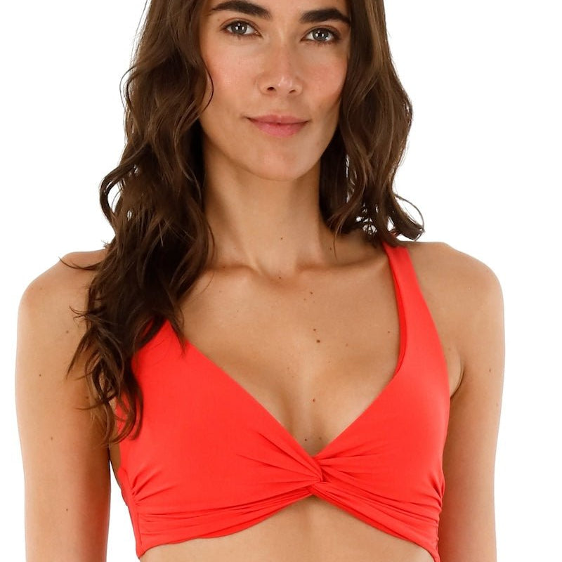 Image of a woman wearing a red swimsuit top by Malai Swimwear. She's smiling and standing on a white background. The purpose of this image is to highlight the bikini.
