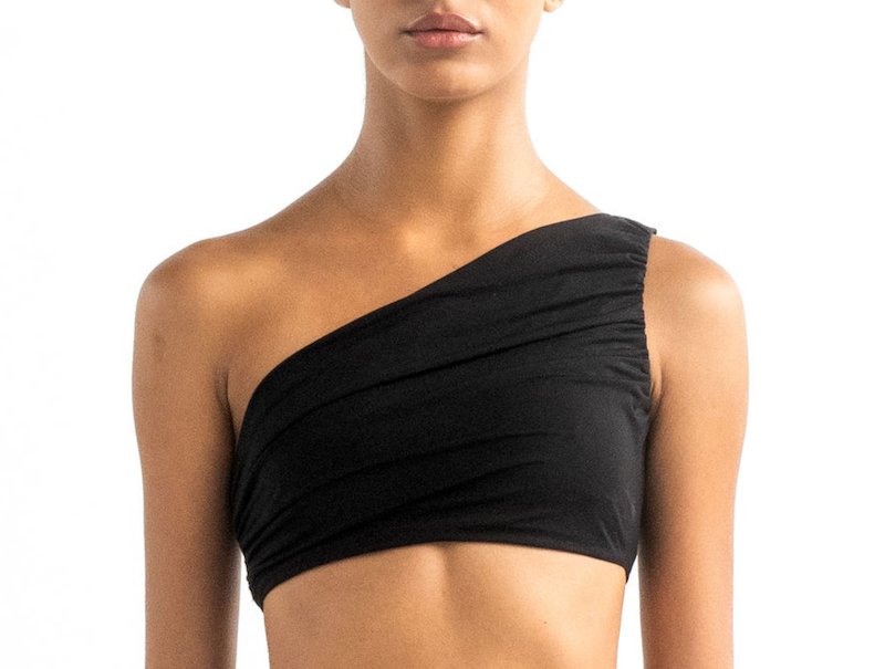 Close-up of a model wearing the Leonor bikini top. It's black and has a drapped one-shoulder look.