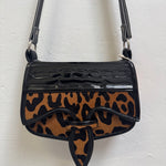 Leopard print handbag with black accents on a white background