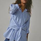 Woman wearing a light blue shirt with a tie-waist design against a neutral background