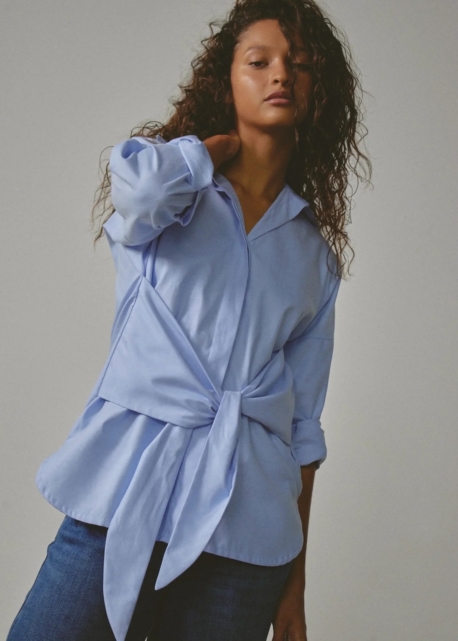 Woman wearing a light blue shirt with a tie-waist design against a neutral background