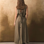 Back of a woman wearing a long olive green dress against a textured brown wall.