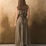 Back of a woman wearing a long olive green dress against a textured brown wall.