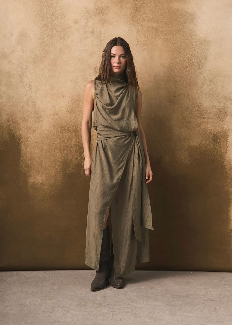 Woman wearing a long olive green dress against a textured brown background