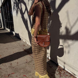 Woman holding a brown leather bag against a light-colored wall.