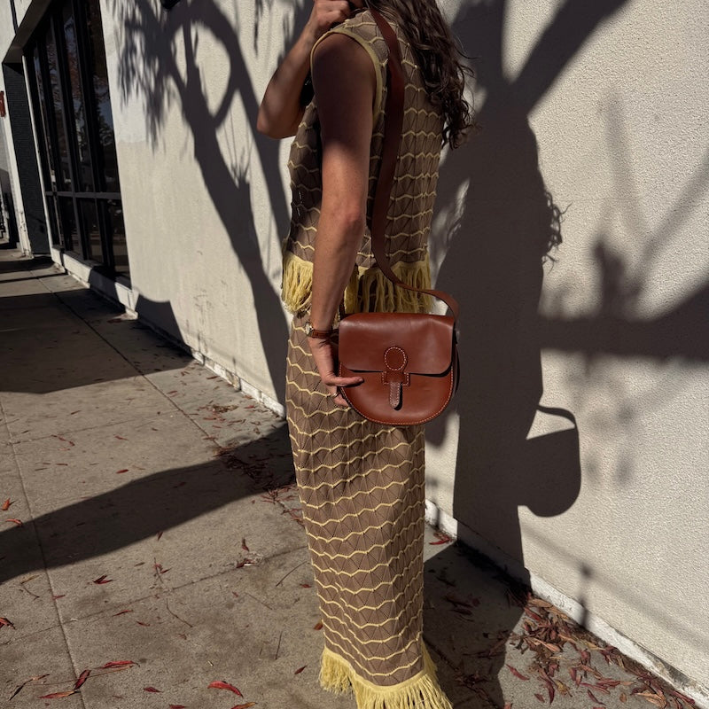 Woman holding a brown leather bag against a light-colored wall.