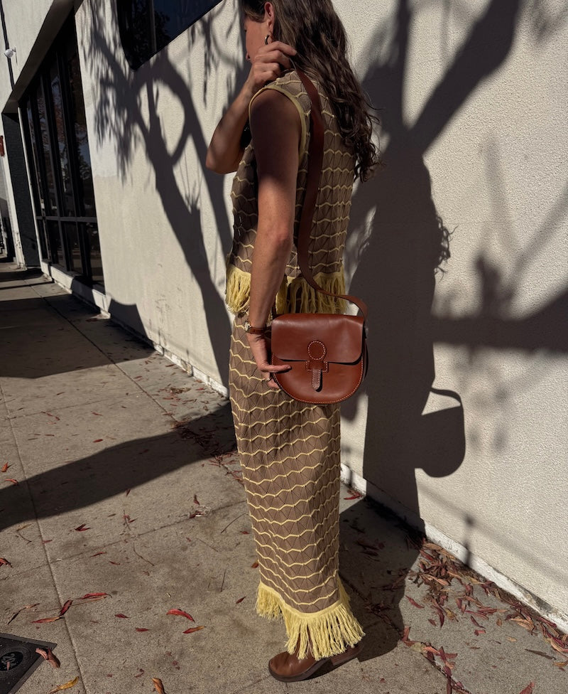 Woman holding a brown leather bag against a light-colored wall.