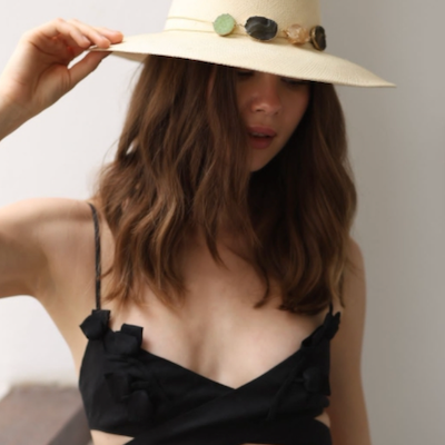 Woman wearing a wide-brimmed hat with decorative crystals against a neutral background