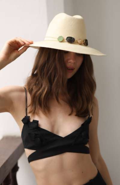 Woman wearing a wide-brimmed hat with decorative crystals against a neutral background
