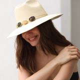 Woman wearing a beige hat with a wide brim and decorative crystals, sitting against a plain background.