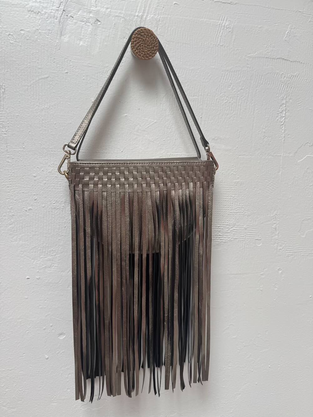 Metallic gold woven handbag with fringe on a white background.