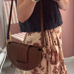 Person wearing a brown leather handbag with a floral skirt and black top.