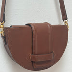 Brown leather handbag with gold hardware on a light gray background.