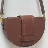 Brown leather handbag with gold hardware on a light gray background.