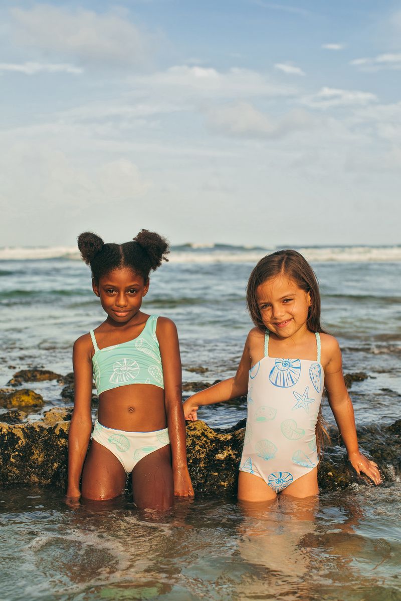 Two young girls in swimsuits standing in shallow water at the beach.