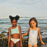 Two young girls in swimsuits standing in shallow water at the beach.