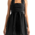Close up image of a woman wearing a black mini halter dress by Encanrtadore Swimwear. It's against a white background. The purpose of this image is to highlight the dress because it is sold at EVAMAIA boutique in Studio City, CA. 