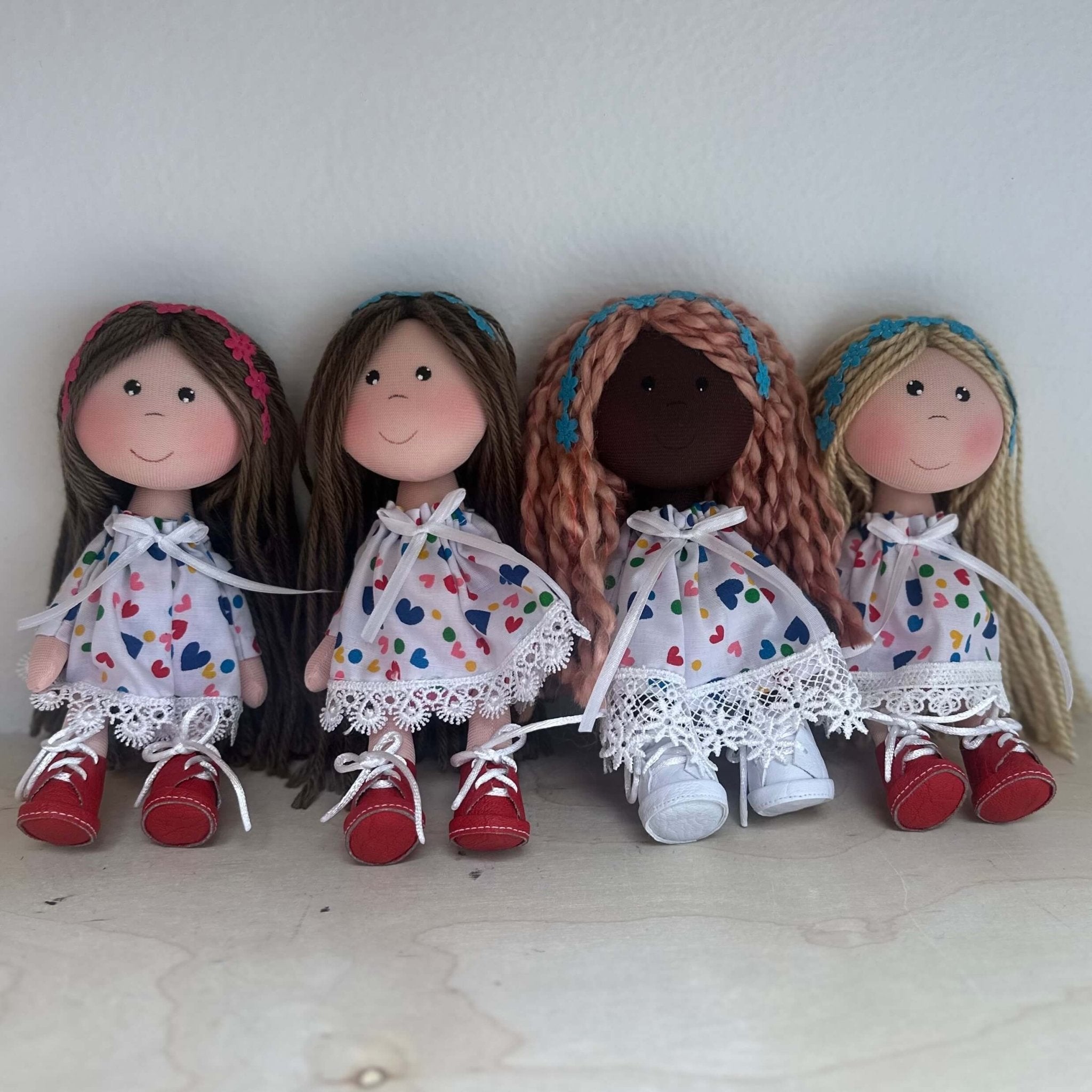 Cute rag dolls handmade in Colombia. There are 4 dolls wearing a white hearts dress with different skin and hair colors. They are also wearing flower headbands.