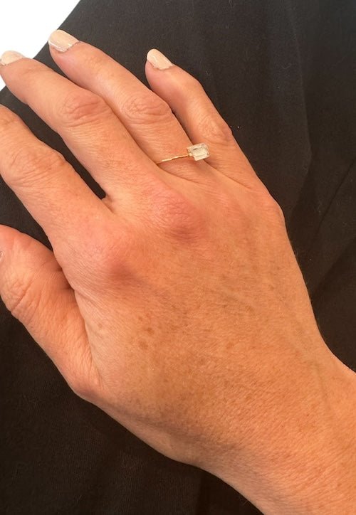 Close up image of a woman's hand wearing a dainty gold ring with a raw quartz stone on it. The purpose of this image is to highlight the ring because it is for sale at EVAMAIA boutique in Studio City, CA and online.