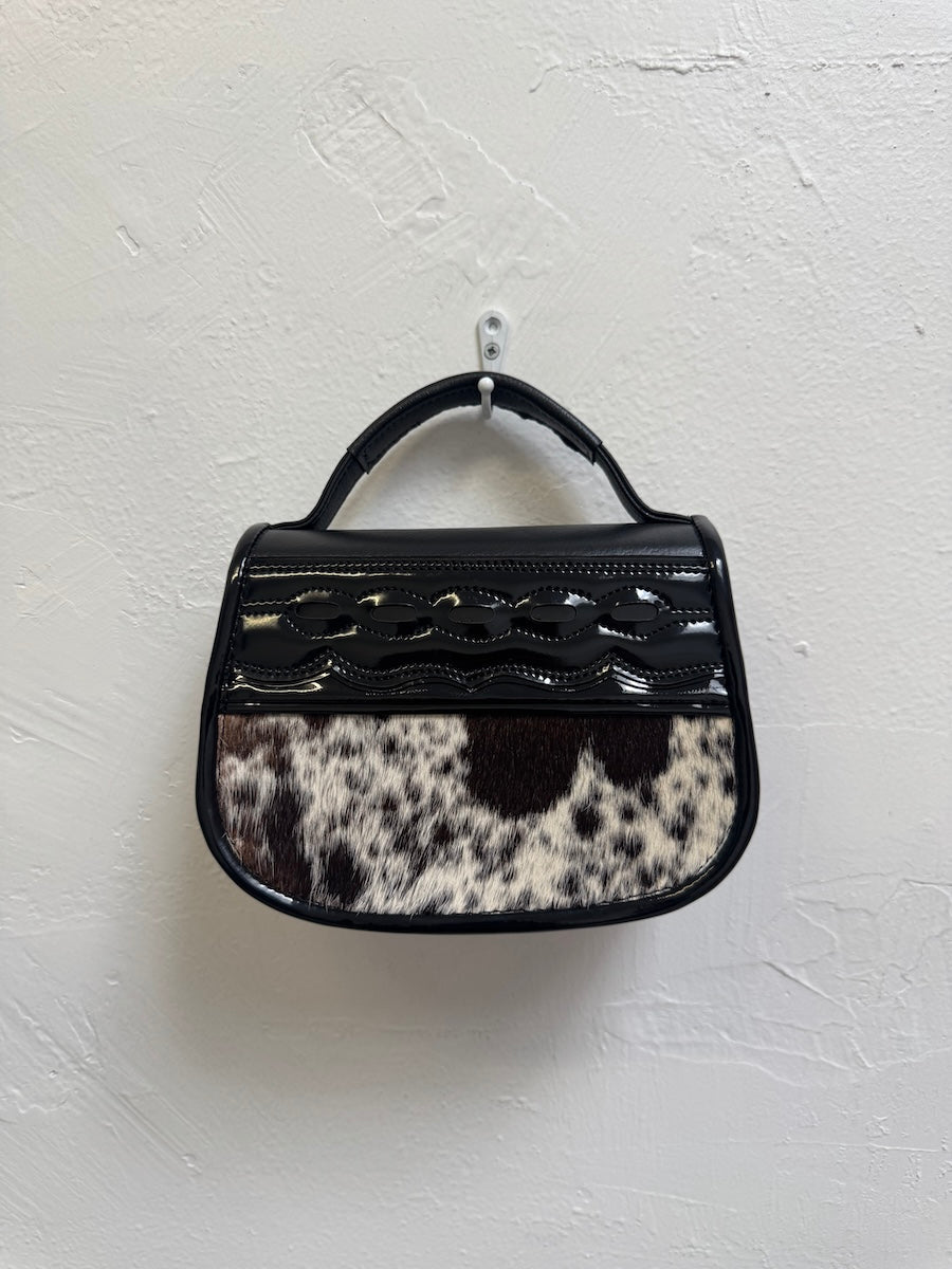 Handbag with black and white cow print pattern on a light gray background