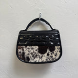Handbag with black and white cow print pattern on a light gray background