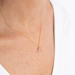 Close up image of a woman wearing a gold necklace with a rose quartz charm. The purpose of this image is to highlight the necklace by Wish Jewelry because it's sold at EVAMAIA boutique in Studio City, CA.