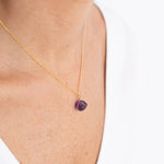 Close up image of a woman wearing a gold necklace with an amethyst charm. The purpose of this image is to highlight the necklace by Wish Jewelry because it's sold at EVAMAIA boutique in Studio City, CA.