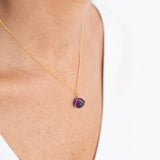 Close up image of a woman wearing a gold necklace with an amethyst charm. The purpose of this image is to highlight the necklace by Wish Jewelry because it's sold at EVAMAIA boutique in Studio City, CA.