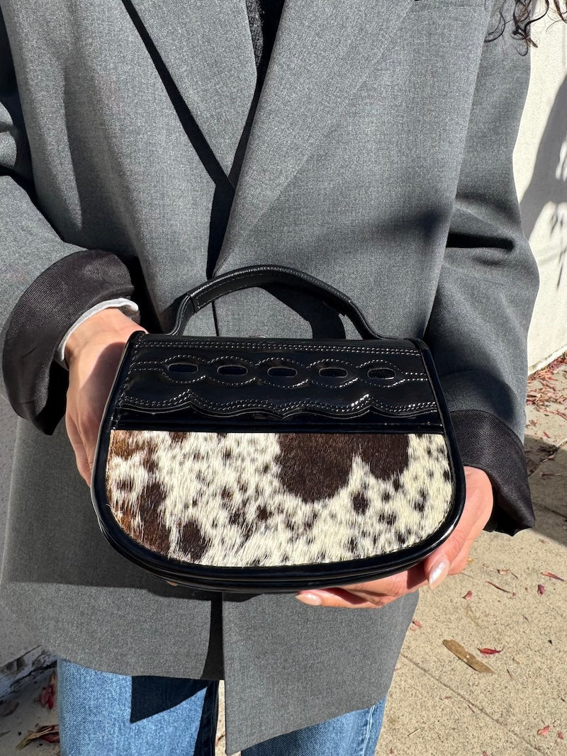Person holding a black handbag with cowhide pattern