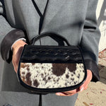 Person holding a black handbag with cowhide pattern