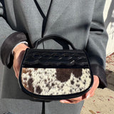 Person holding a black handbag with cowhide pattern