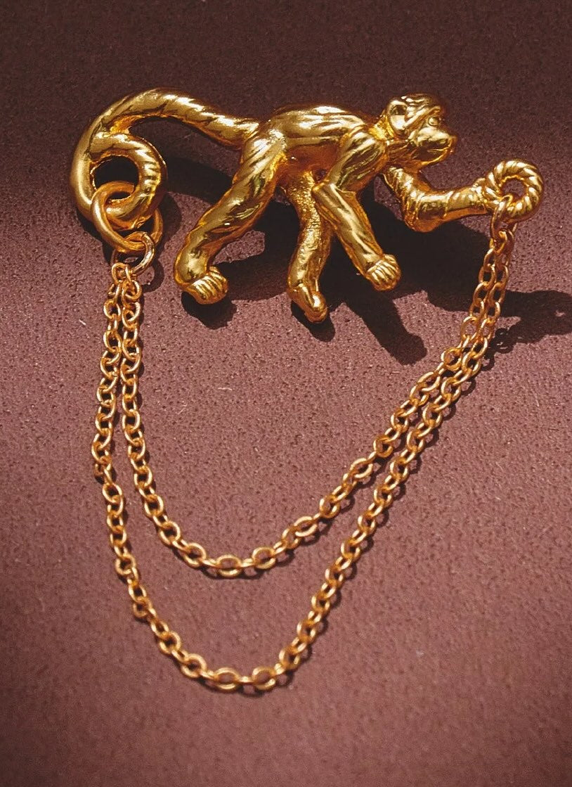 Gold monkey brooch with chain on a brown background