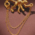 Gold monkey brooch with chain on a brown background