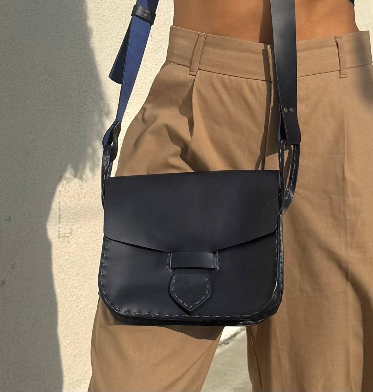 Person wearing a black leather satchel bag over one shoulder against a neutral background