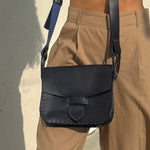 Person wearing a black leather satchel bag over one shoulder against a neutral background